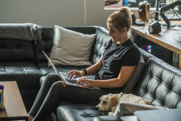 Woman with a small dog working on a computer on a couch