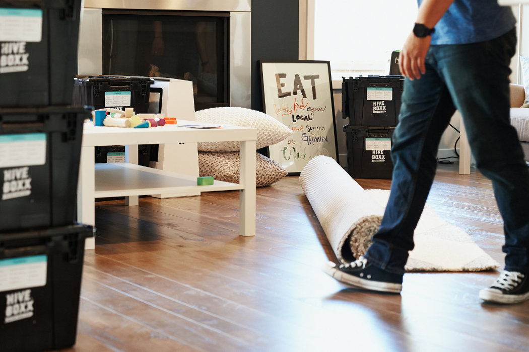 A person walking past a rug and furniture waiting to be set up in a room.