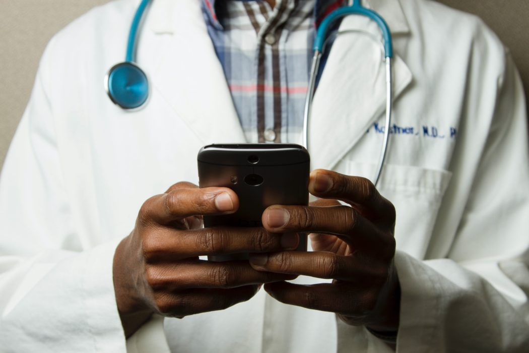 A doctor's hands use a cell phone to interact with someone.