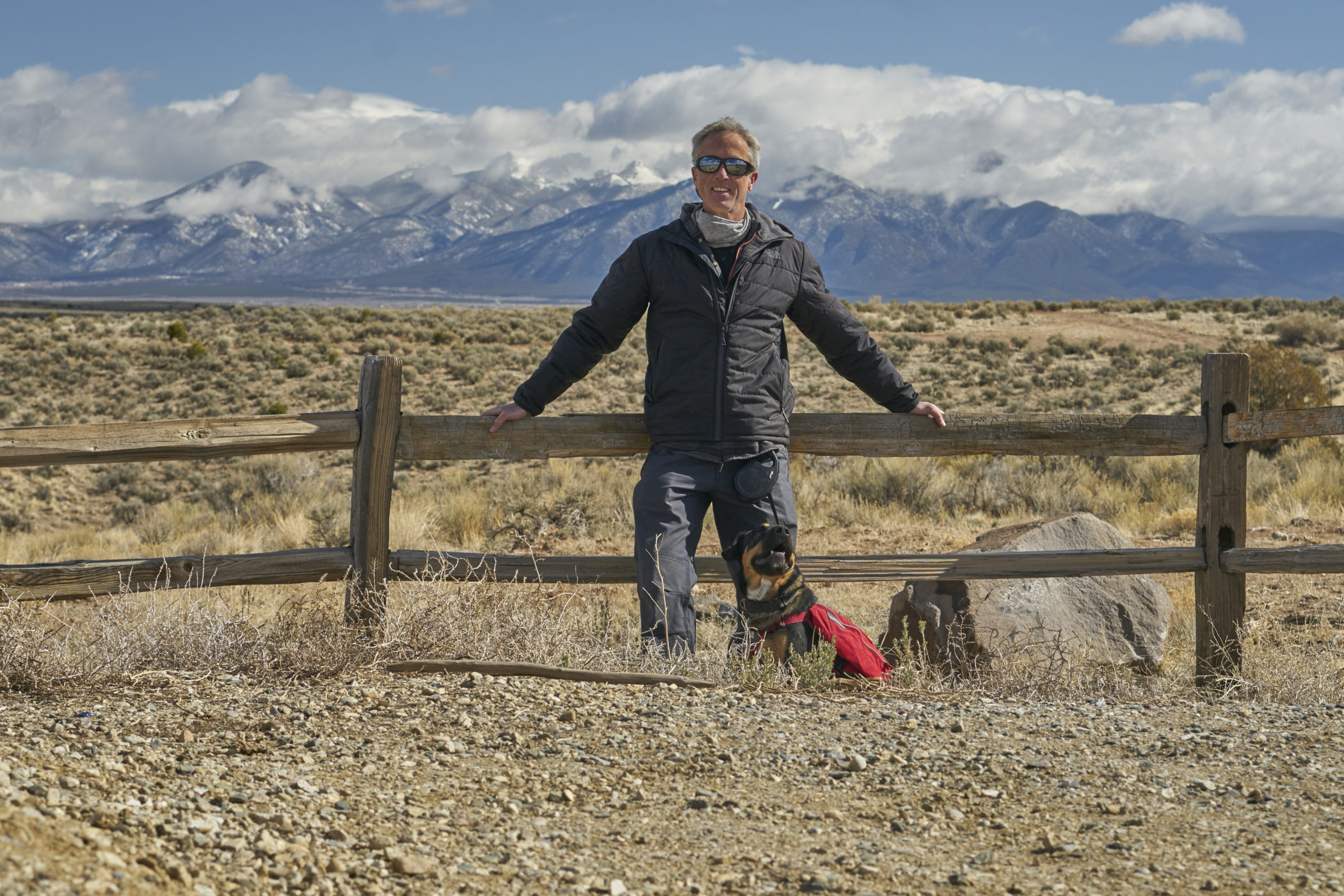 Peter Walker and his dog rest near a fence in the high desert near Taos