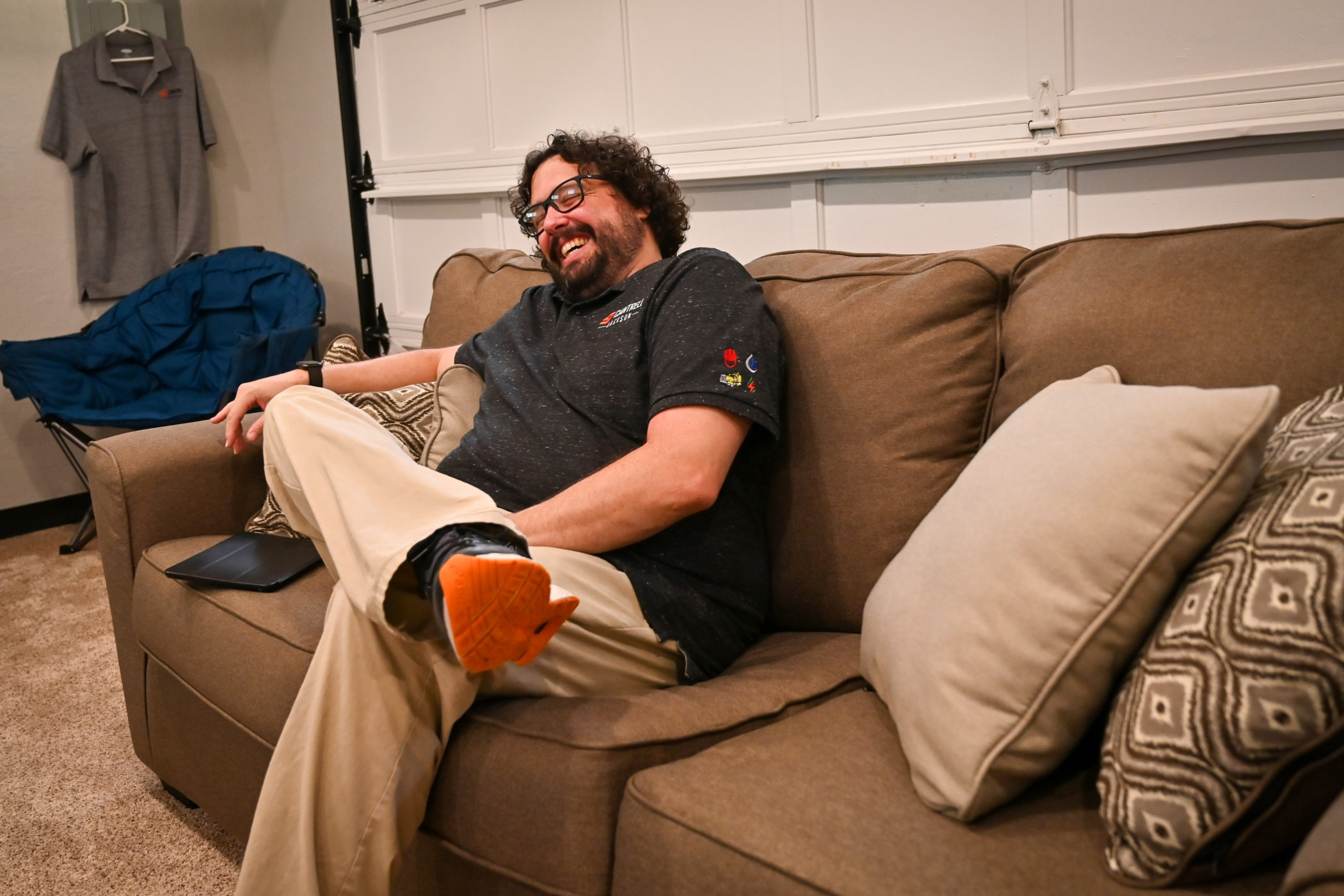 Jake Cantrell laughs while sitting on a brown couch in his office