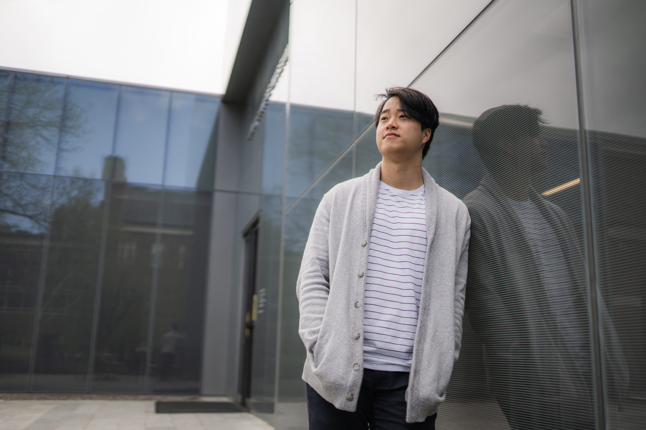 Josh Kim leaning against the glass windows of a building at Colby College in Waterville, Maine